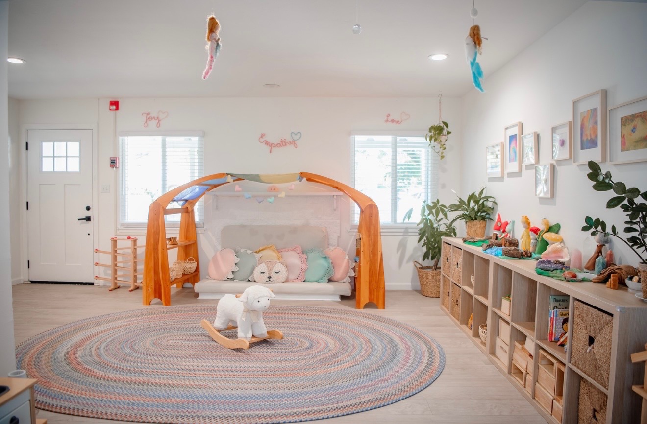 The main indoor playroom with a wooden canopy daybed, natural toy shelves, and a lamb rocker on a round braided rug