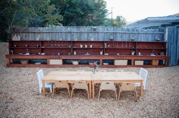 An outdoor wooden mud kitchen and a child-sized table on a soft wood-chip play area