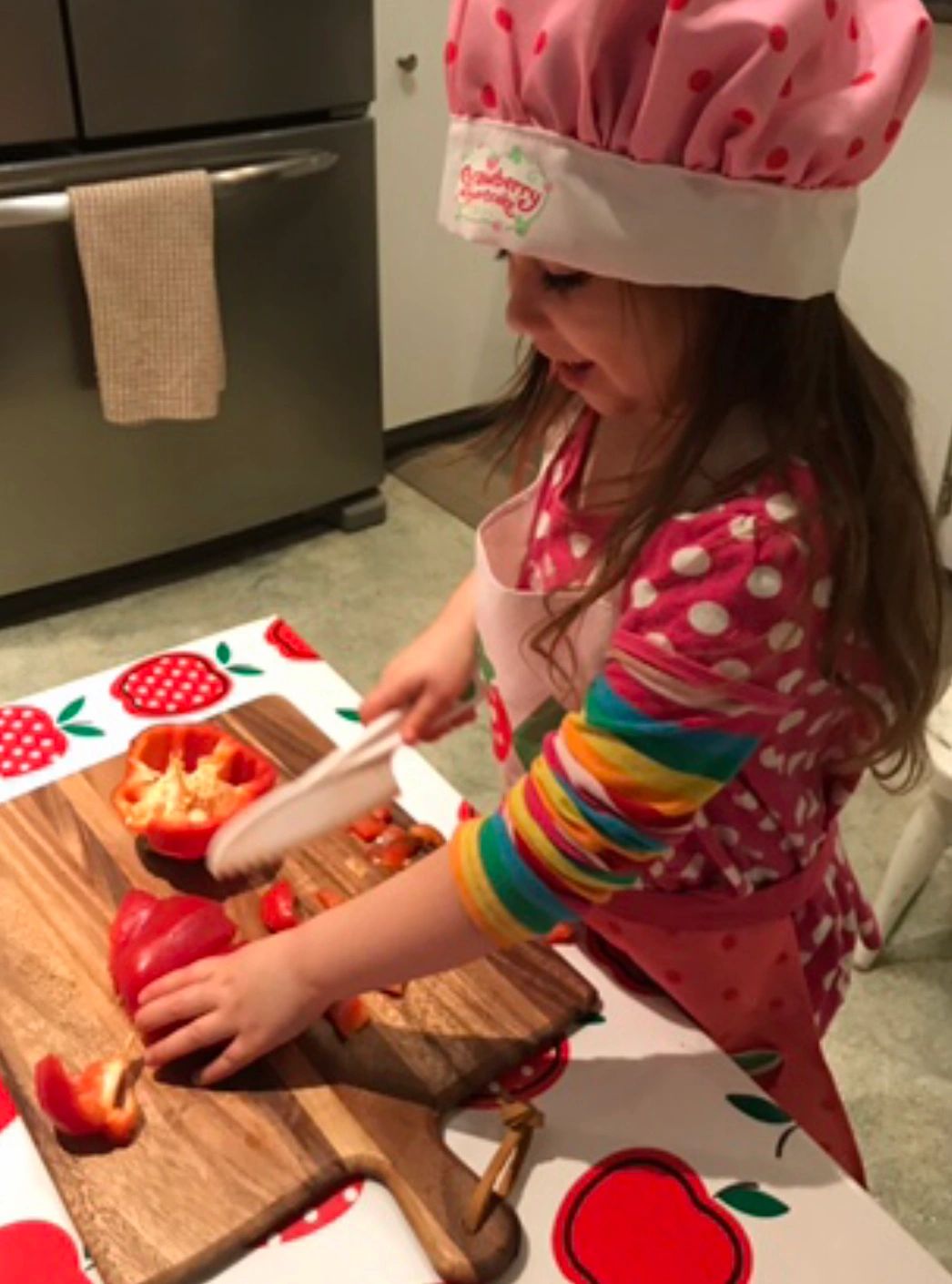 A child in a chef's hat preparing vegetables