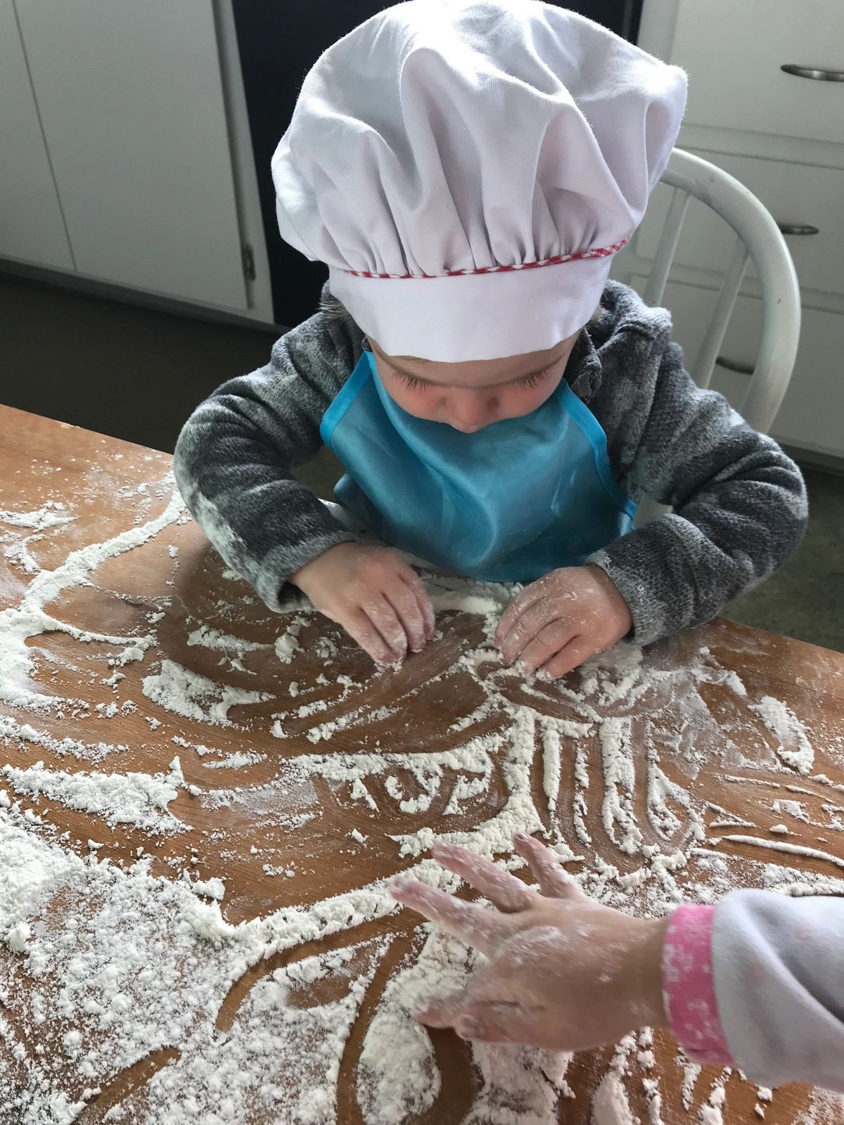 A child in a chef's hat kneading bread dough