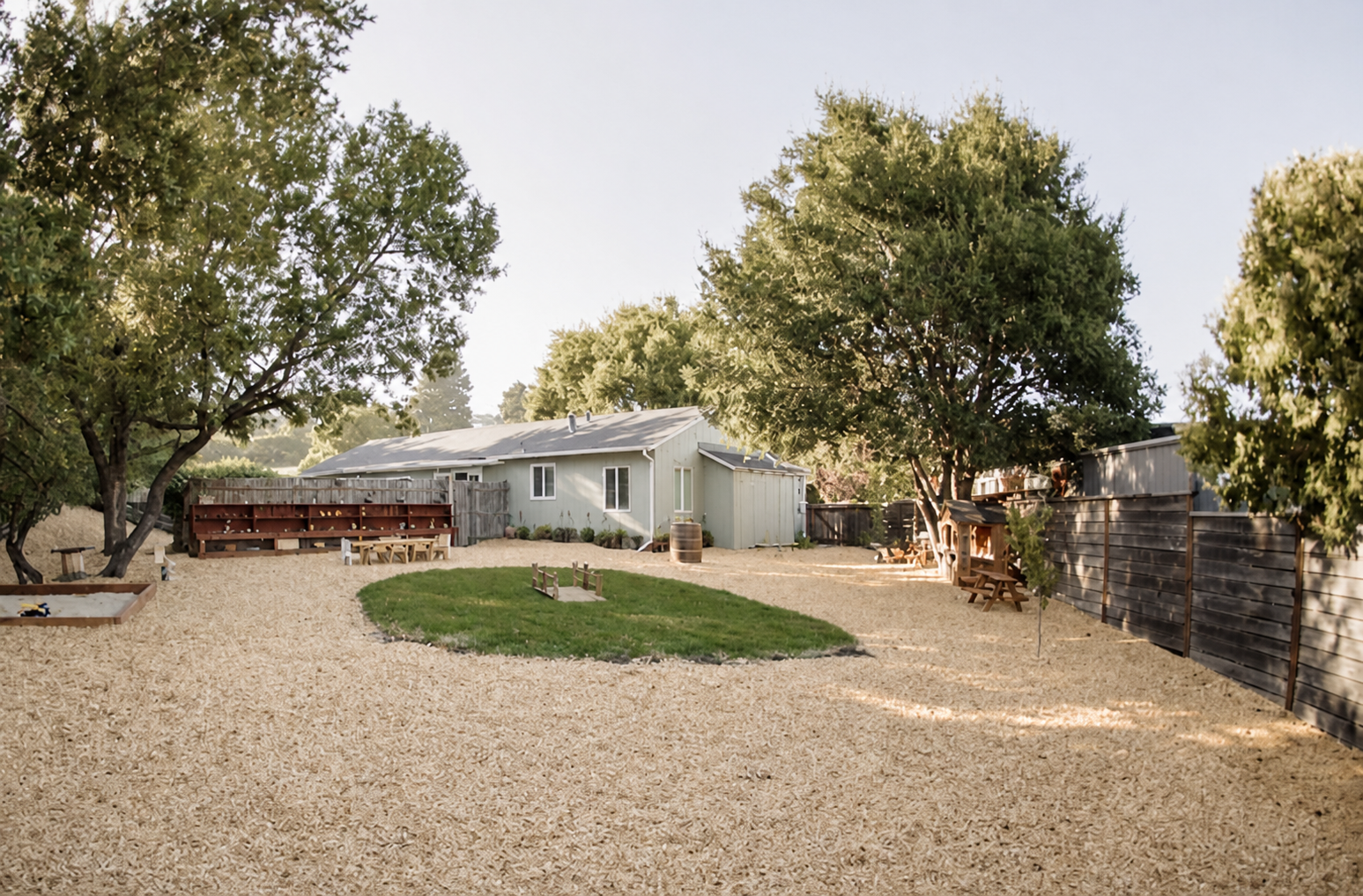 A wide view of the backyard with trees, a grass circle, and wood-chip play areas