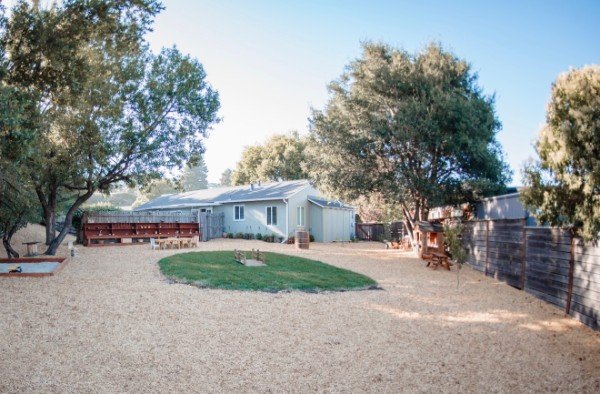 A wide view of the backyard with trees, a grass circle, and wood-chip play areas