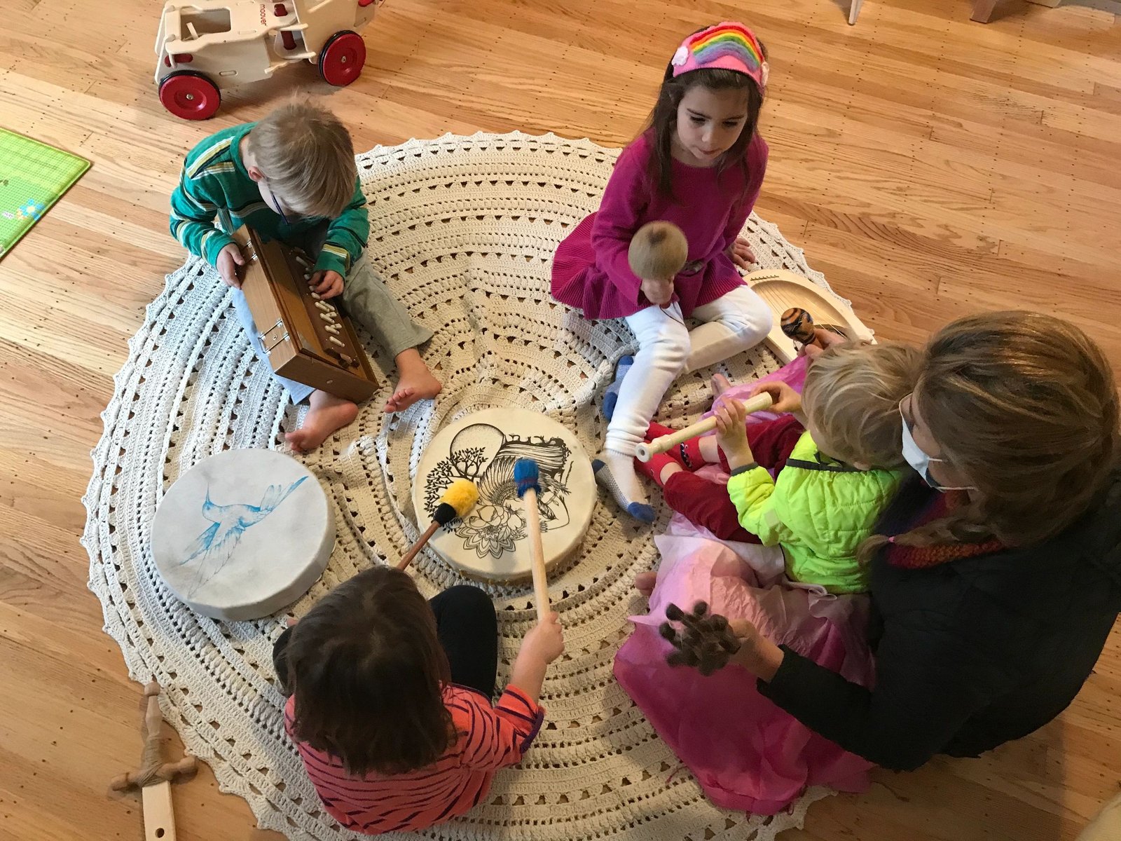 Children playing hand drums with their teacher on a round rug