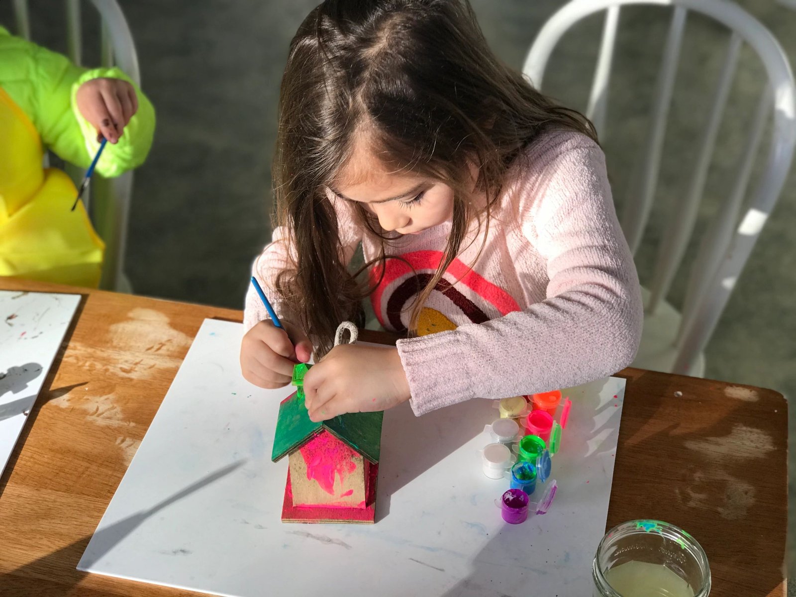 A child painting a wooden birdhouse at the craft table