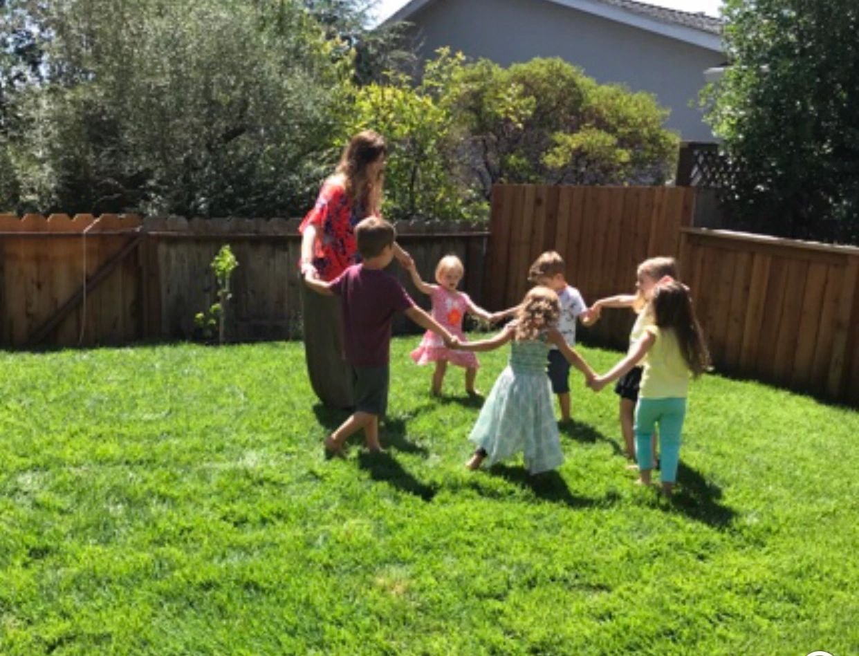 Children and a teacher playing a ring game on the grass