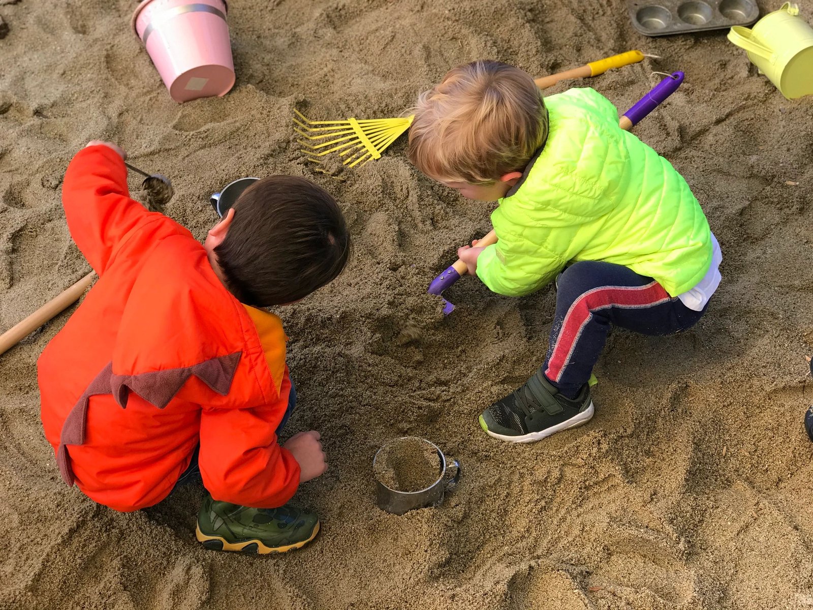 Two children digging in the sandbox with rakes and tools