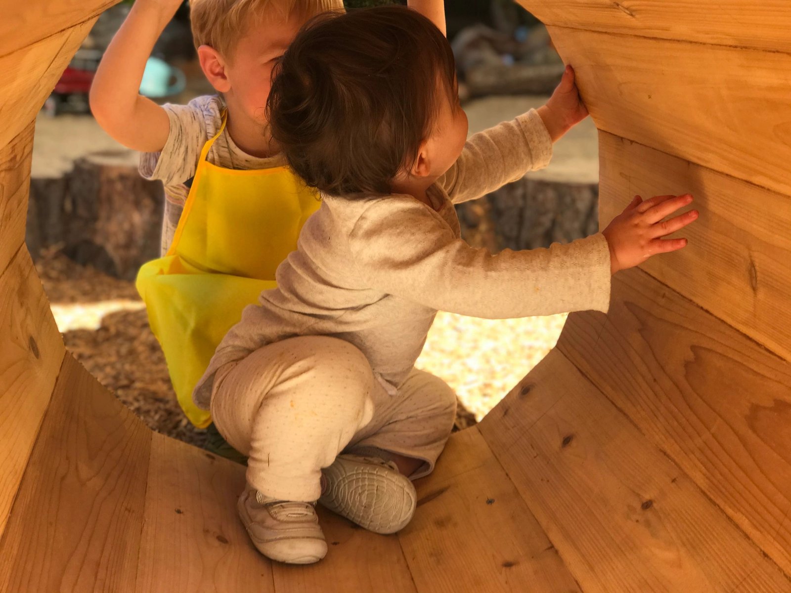 Two children peeking through a wooden play structure outdoors
