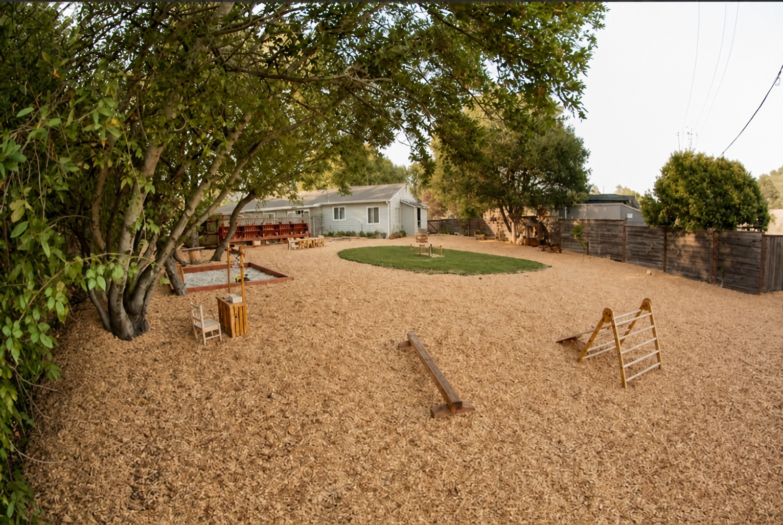 The play yard with wooden balance beams and a climbing ladder on the wood chips