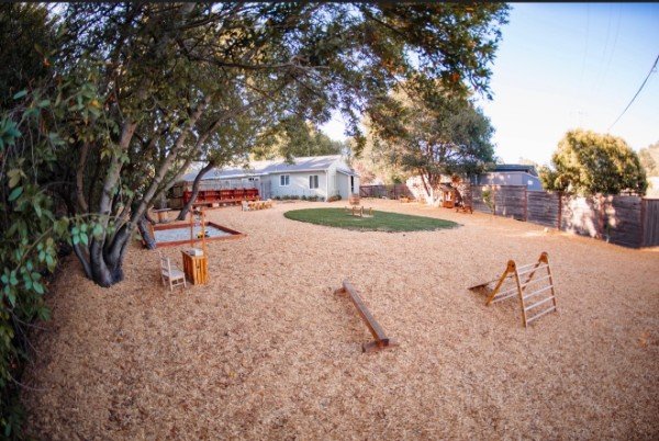 The play yard with wooden balance beams and a climbing ladder on the wood chips