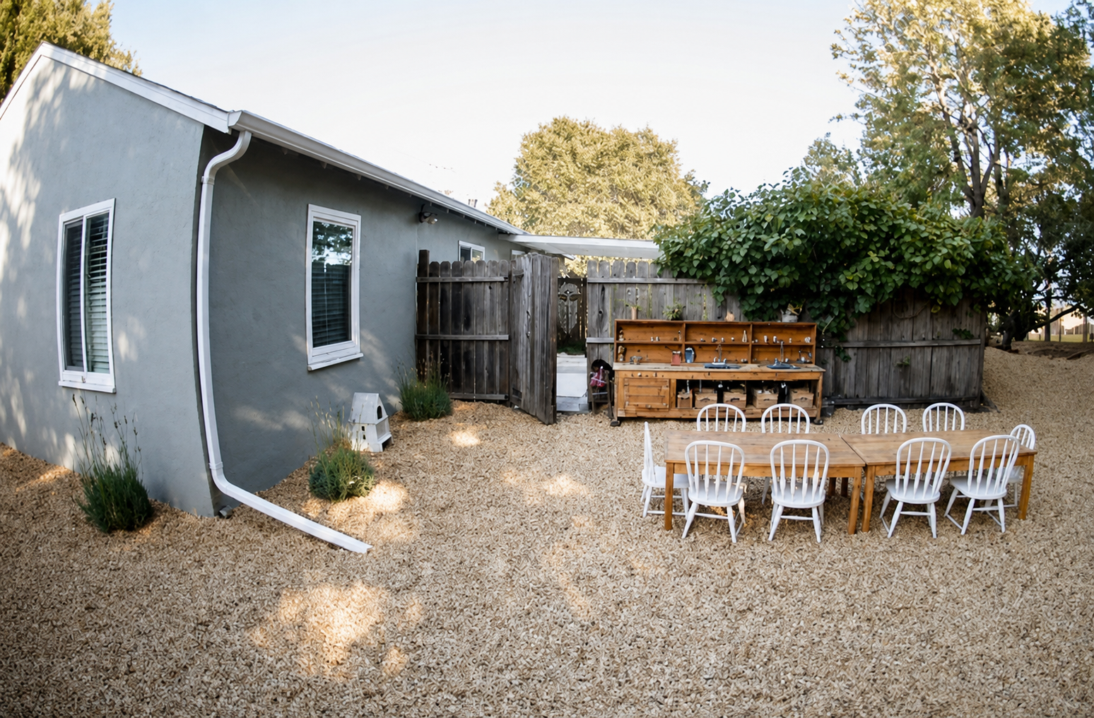 The outdoor play yard with a long wooden table and the mud kitchen along the fence